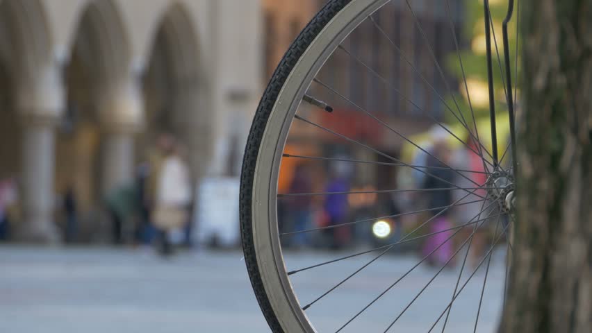 Close up shot of parked bicycle with wheel spokes and peopla walking in the oldtown in the background.