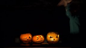 Amusing child playing as vampire close illuminated pumpkins, funniest Halloween video, dark background