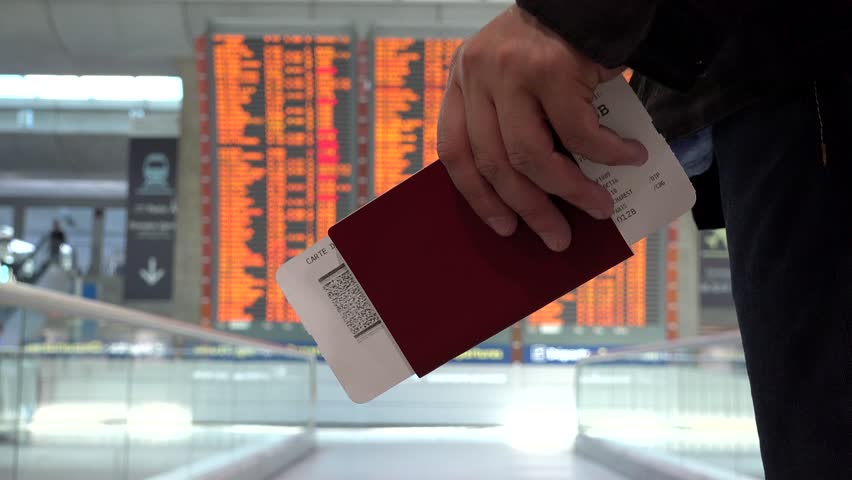 Man holding a passport in his hand going close to big timetable schedule screen, looking information in the airport about arrivals and departures terminal gate to his destination