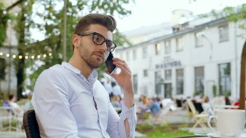 Bored man mimic the person he speaks to through cellphone in the outdoor cafe
