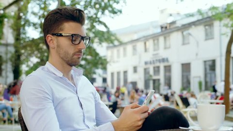 Happy man relaxing in the outdoor cafe and browsing internet on smartphone
