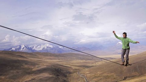 Slackliner balancing on tightrope between two rocks, Snowy mountains of the Huascaran park on the background, Peru. Slow motion