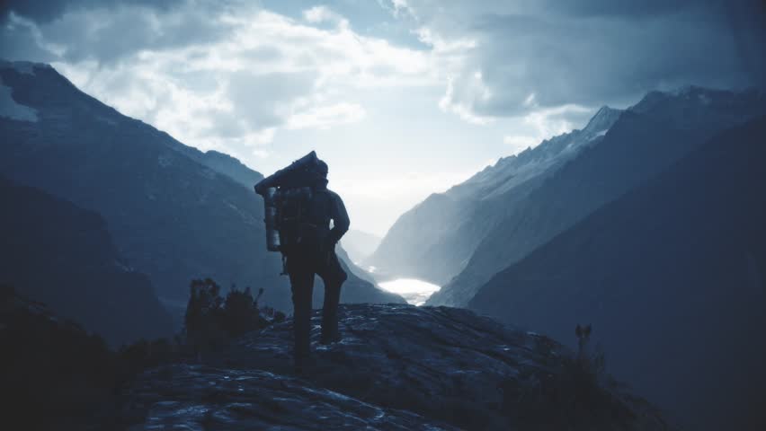 Silhouette of backpacker walking towards the edge of a rocky peak to contemplate the beautiful panorama of the Huascaran National Park. Slow motion