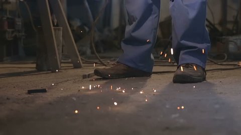 Welder welds metal. Close-up sparks falling on shoes