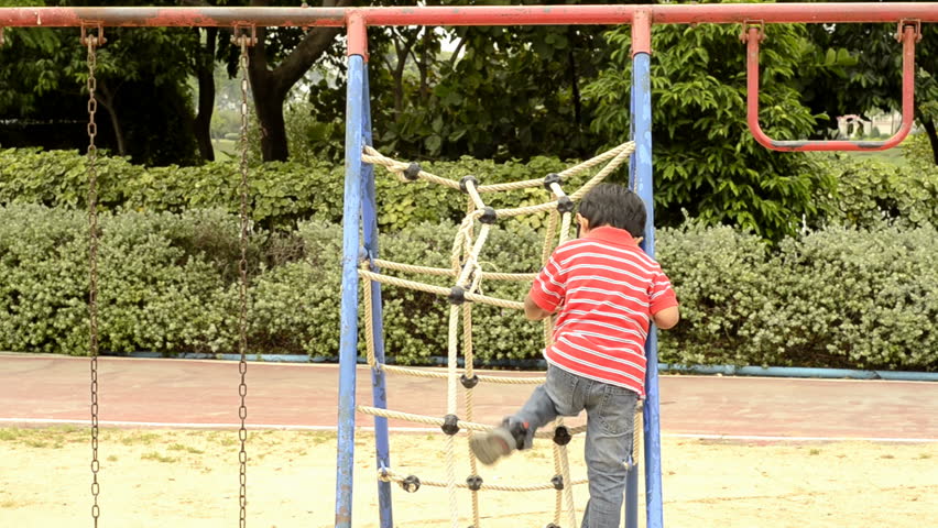 Young boy climbing up a rope ladder in a playground.