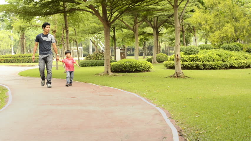 An Asian father points something out while walking in the park with his son.