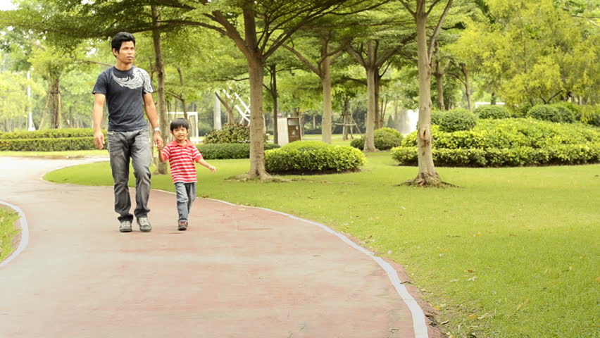 An Asian father points something out while walking in the park with his son.