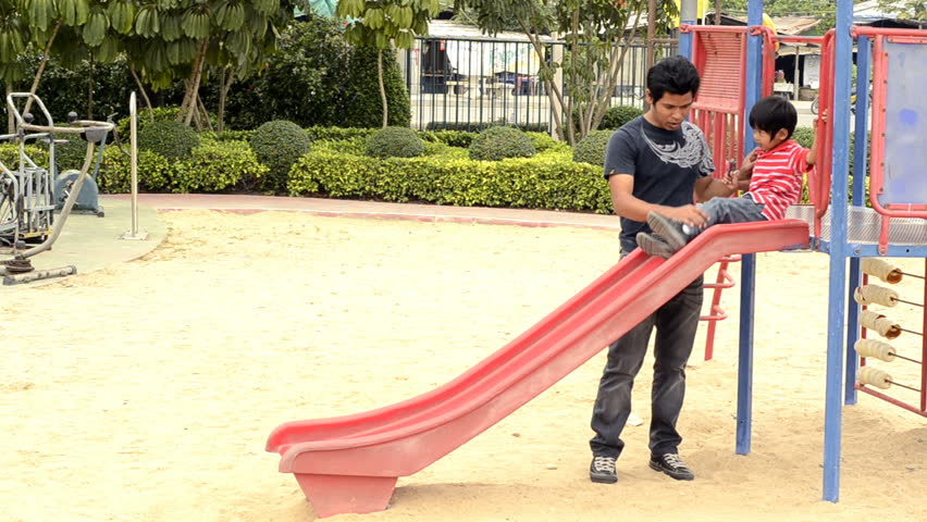 An Asian father and son playing together on a slide in a park.