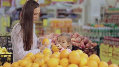 Young mother and cute baby daughter in supermarket buying fruits and vegetables