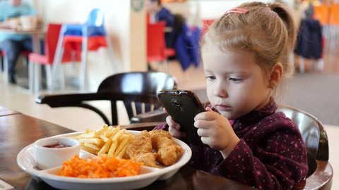 Little kid girl make dish photo via smart phone during eating in fast food court in a mall