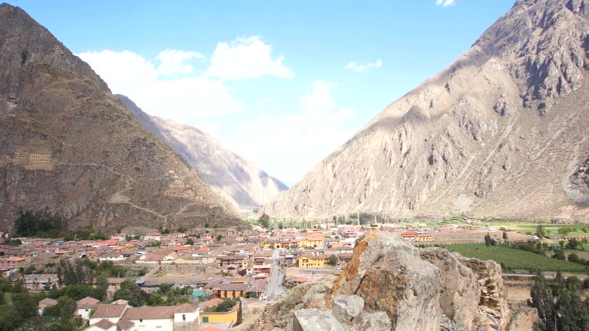 Full pan shot of Ollantaytambo, Peru, with the mountains and blue sky framing the town.