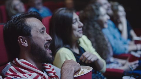 Closeup of young couple sharing popcorn while watching comedy in movie theater