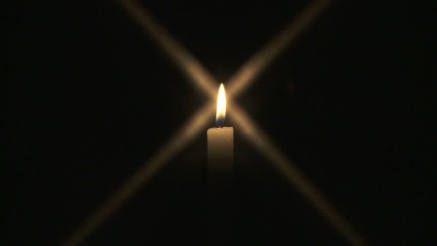 Wide shot of single candle burning in the dark