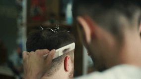 young barber trimming man's hair with scissors in barbershop