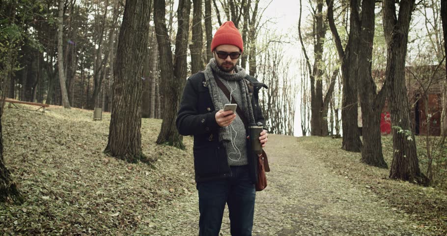  Young man  goes and listen to music from earphone in park and drink tea