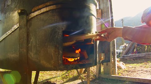 Man putting wood the in cauldron and makes fire for baking domestic brandy