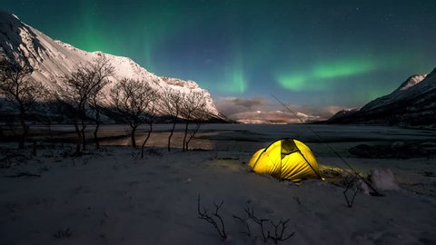 Northern Lights over an illuminated tent in a norwegian fjord in winter.