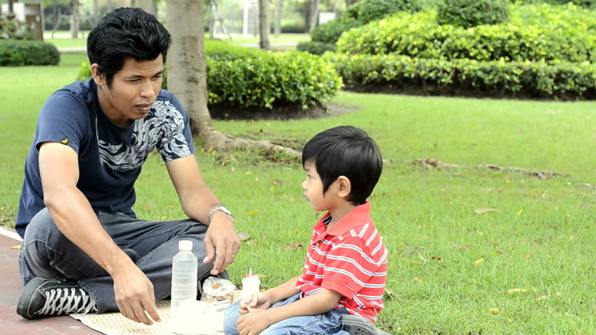 An Asian father and son having a picnic together in a park.