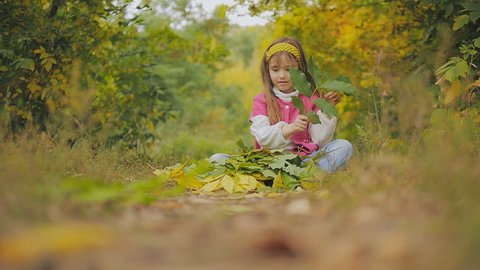 little girl sitting on the footpath and fun throws autumn leaves. Slow-motion