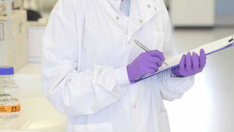 Portrait of Female writing down notes on notepad in science laboratory and looking to camera