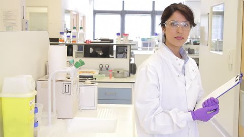 Portrait of Female writing down notes on notepad in science laboratory and looking to camera
