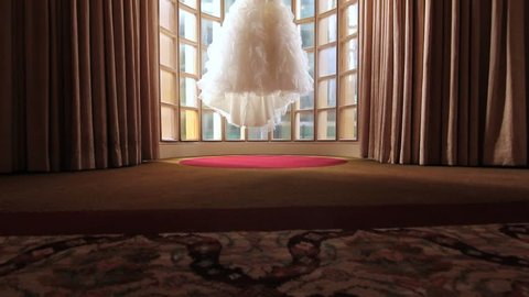 A bride's wedding gown hanging in the middle of a beautiful bay window.