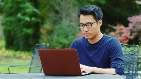 Asian man wearing glasses works with a laptop. Sitting on the summer terrace in the gardens or cafes.
