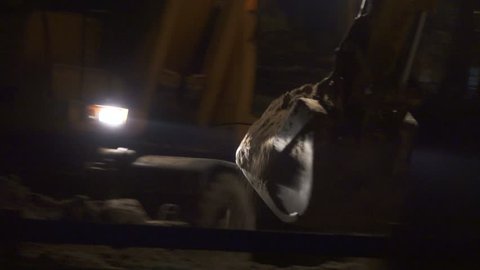 Excavator with headlights digging trench at night