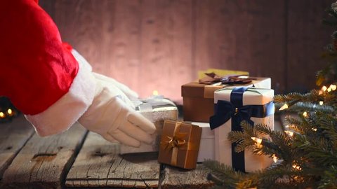 Santa Claus putting gifts under the Christmas tree with blinking garlands. Santa Claus giving gift box, holding a gift in his hands over wooden background.  Full HD 1080p video footage