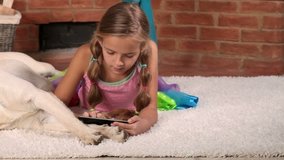 Little girl playing on tablet computer laying with her labrador dog  - closeup, slide
