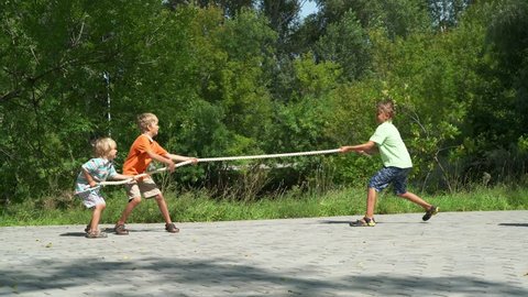Three happy boys playing tug-of-war in park. Kids pull the rope in sunny day. Summer fun.