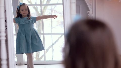 little girl in blue dress looking in the mirror and admiring herself