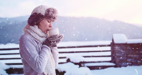 Woman drinking Hot Tea or Coffee from Festive Cup with Snowy Mountain View on Background. 4K SLOW MOTION 120fps. Beautiful Girl Enjoying Winter Morning or Evening Outdoors. Christmas Holidays