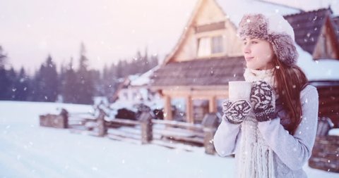 Woman with Cup of Hot Tea or Coffee by the Cozy Mountain Cottage on Snowy Winter. 4K SLOW MOTION 120fps. Beautiful Girl Enjoying Winter Outdoors, drinking from a Mug, getting warm. Christmas Holidays