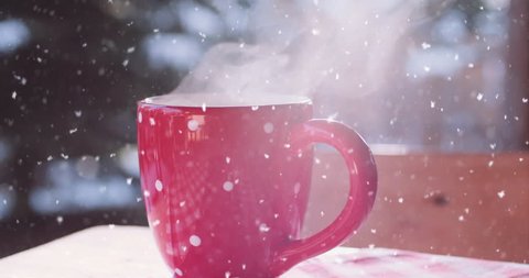 Steaming Cup of Hot Coffee or Tea standing on the Outdoor Table in Snowy Winter Morning. 4K DCi SLOW MOTION 120 fps. Cozy Festive Red Mug with a Warm Drink in Winter Garden. Christmas Morning Concept