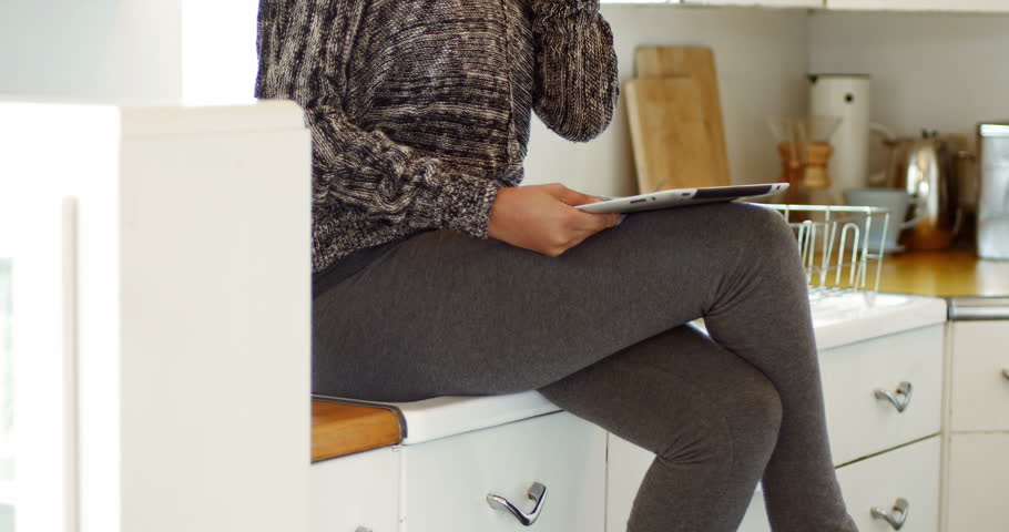 Woman talking on mobile phone while using digital tablet in kitchen at home