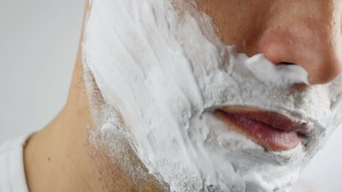 Man shaves his face. Man shaving with foam and manual razer. Close up of man shaving beard.