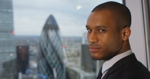 4k, Portrait of a confident African American businessman standing in an office with London skyline in the background. Slow motion.