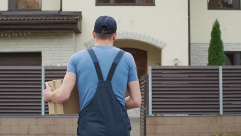 Delivery Man Comes To the Suburban House Door and Knocks. Camera Follows Him from the Back. Shot on RED Cinema Camera in 4K (UHD).