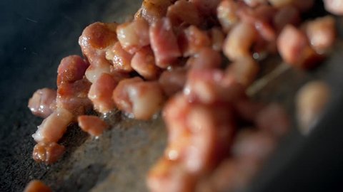 A woman is cooking bacon dices in a frying pan. Tasty food with smoke and frying oil. Very closeup slow motion shot 