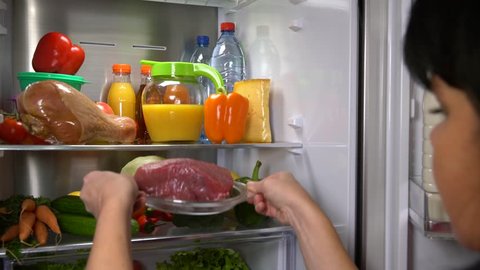 Woman takes meat of beef from of fridge. Healthy eating. Vegetables and fruits in summer season. Refrigerator full of food. 4K