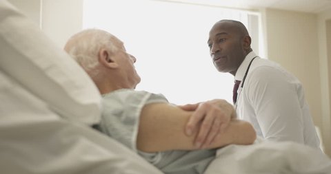 4K Friendly doctor comforting elderly patient at his bedside (UK-Oct 2016)