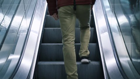 Close-up shot of young man with bag moving on escalator,  traveling on train. Rush hour, subway underground station. Modern escalator stairs moving up.
