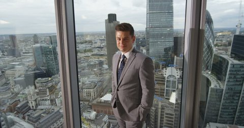 4k, Portrait of a confident businessman standing in an office with London skyline in the background. Slow motion.