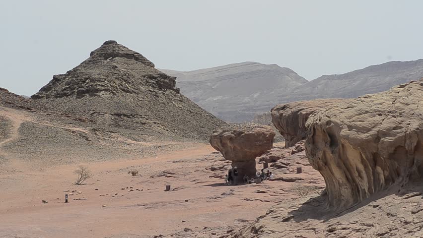 People stand in shade under geological formation in desert valley of Timna park, Israel 