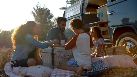 Family eating picnic outside their camper van at sundown