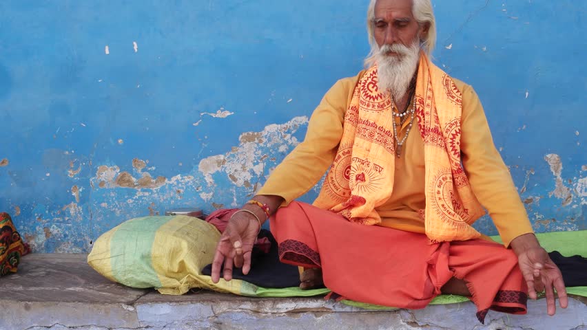 Dolly in to Sadhu, Indian saint, sitting outside a temple in meditation against a blue wall Royalty-Free Stock Footage #21595771