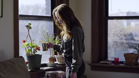Young Woman Waters Her Plants In Her Trendy City Apartment