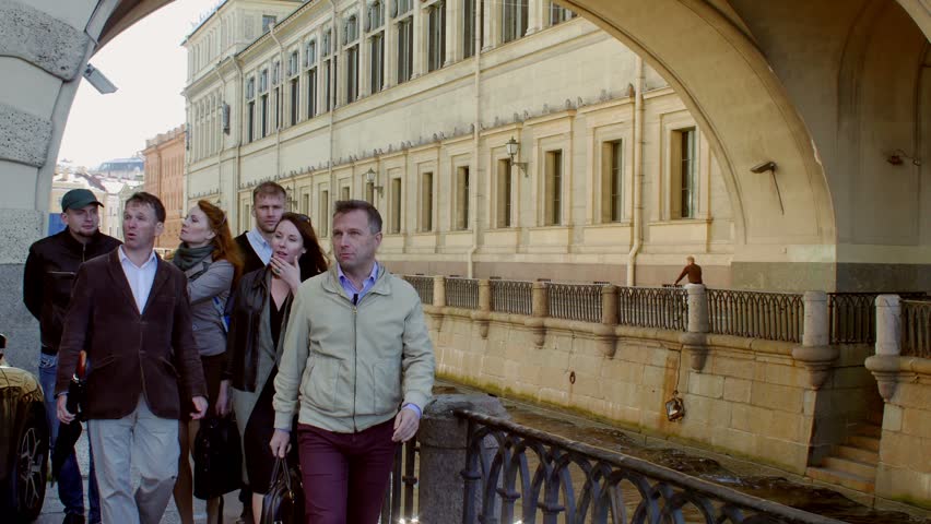 Tourist group with guide come close to the camera and look at the object behind. Background of old building with arch