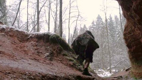Prehistoric caveman goes outside from his cave on a background of winter forest